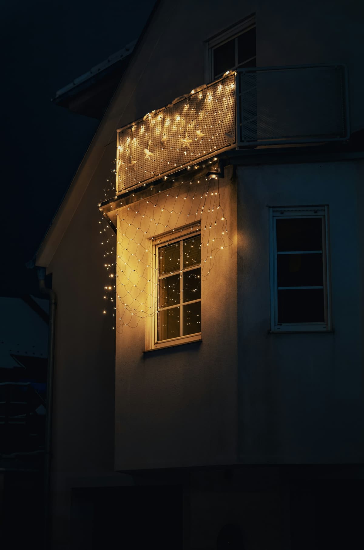 Corner of a house at night with warm white lights along the eaves above a lit window